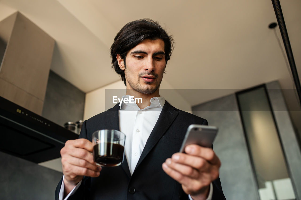 Businessman holding coffee cup while using mobile phone
