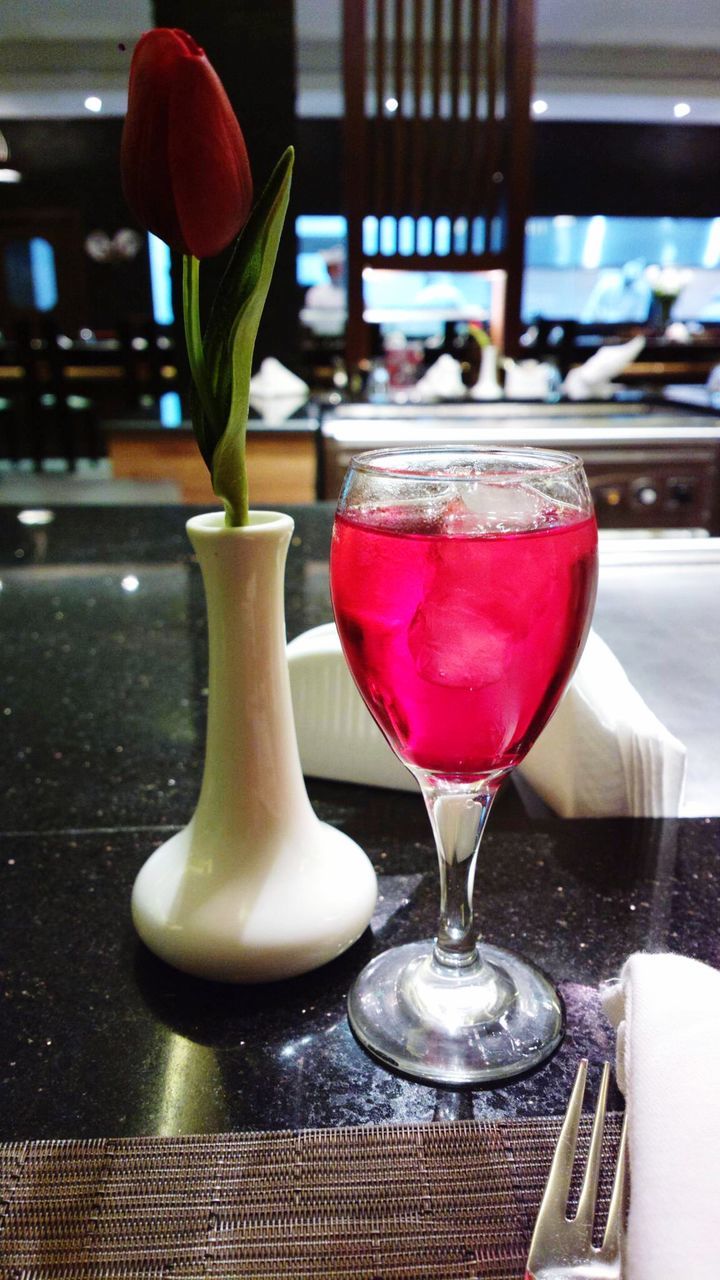 Fresh tulip in vase with cold drink on table