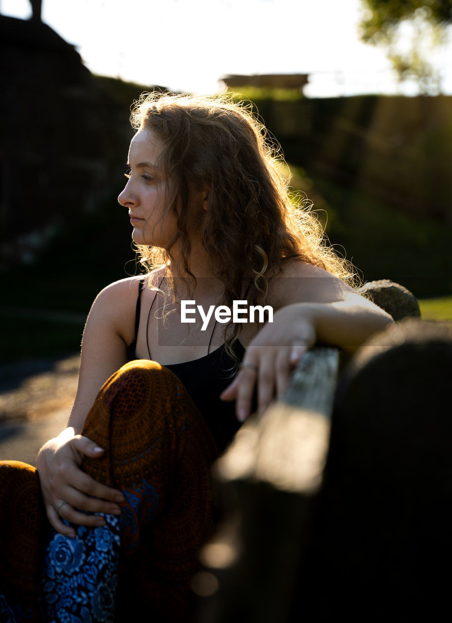 Young woman looking away while sitting outdoors