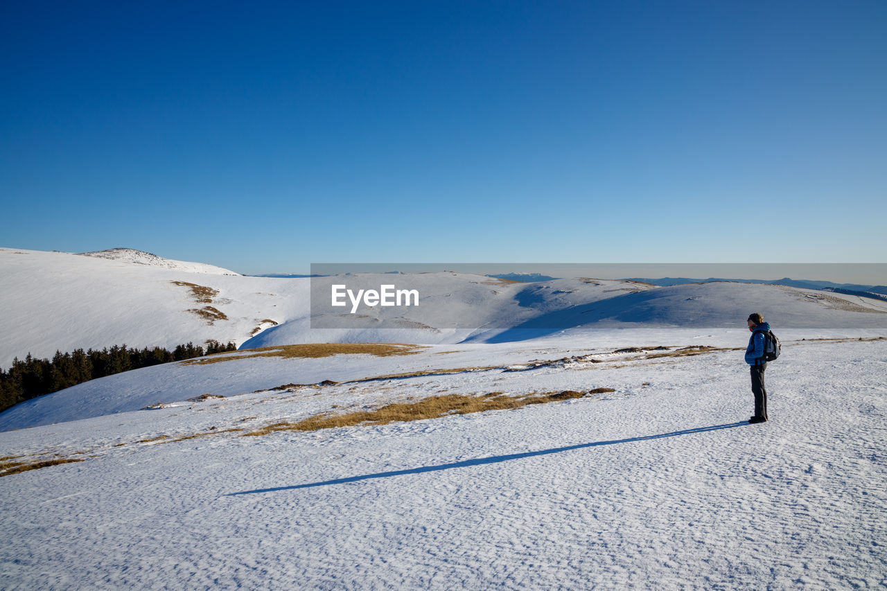 WOMAN ON SNOWCAPPED MOUNTAIN AGAINST CLEAR SKY