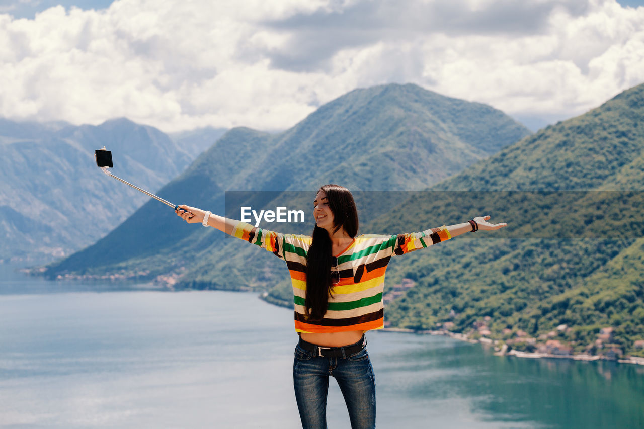 Woman taking selfie while standing at lake against mountains