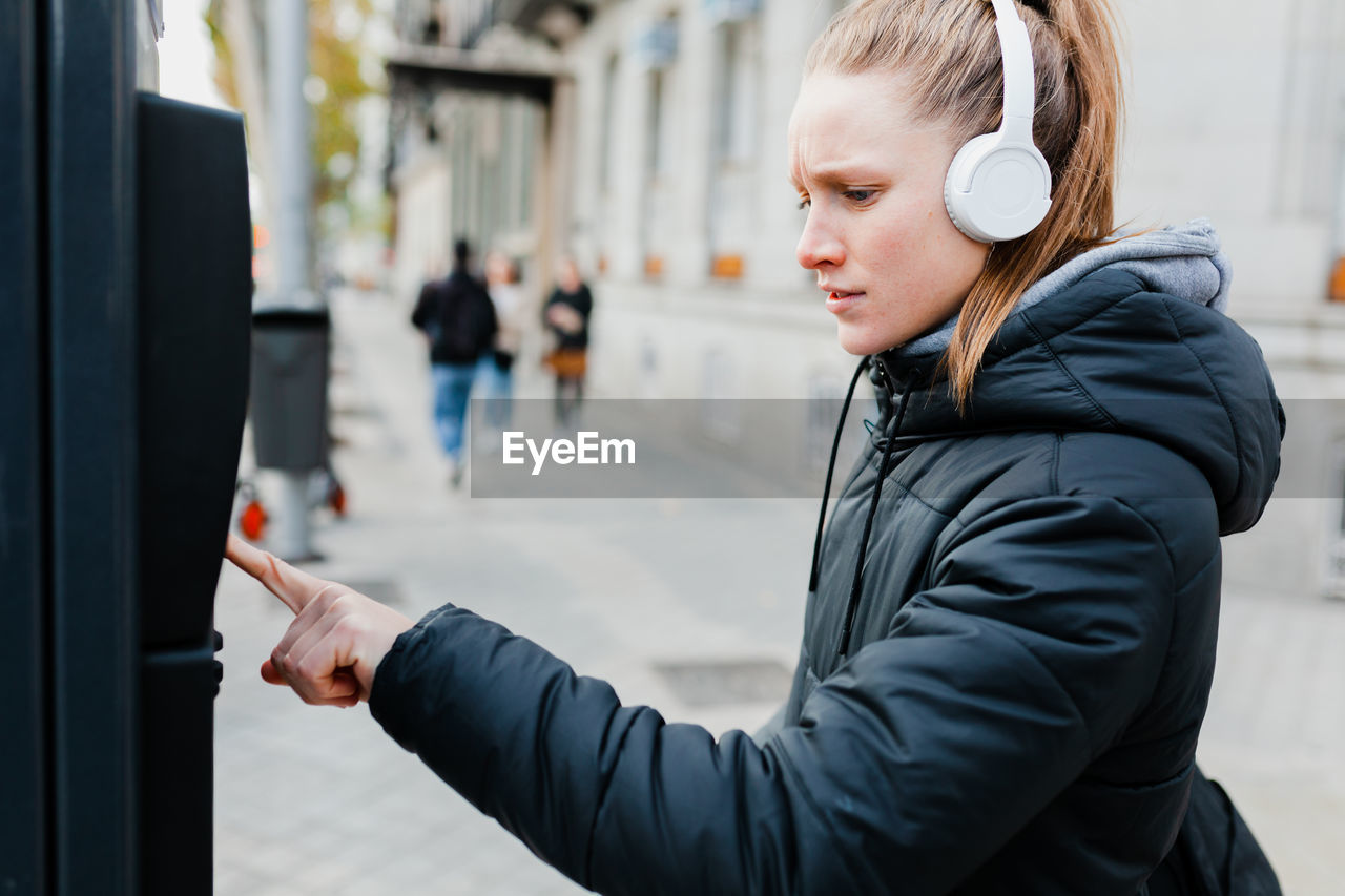 Young woman listening to music using parking meter