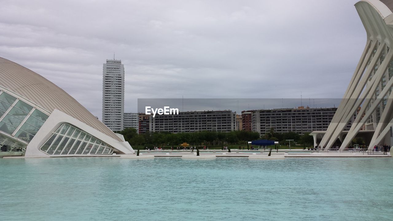 MODERN BUILDINGS BY SWIMMING POOL AGAINST SKY