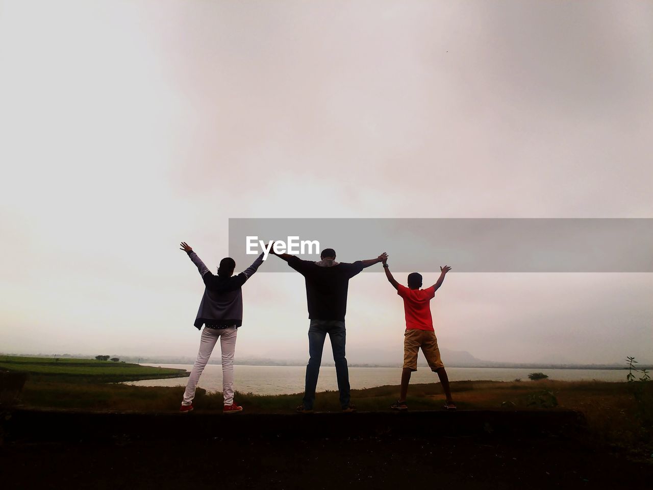 Rear view of people with arms raised standing on land against sky