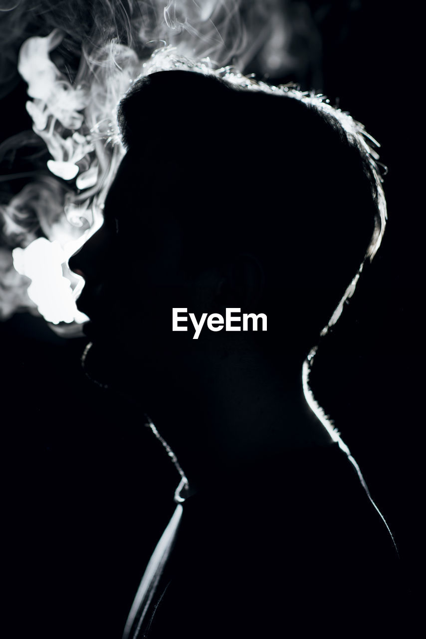 Side view of man smoking cigarette at night