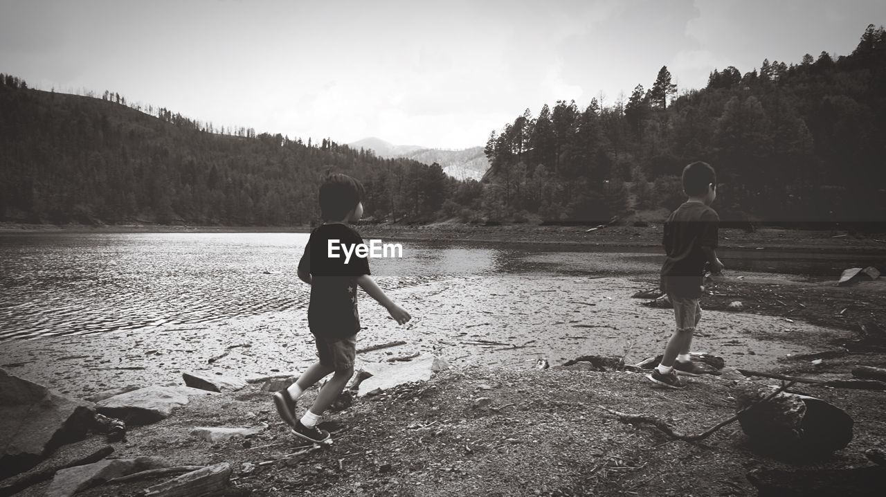 Rear view of boys running by lake against sky