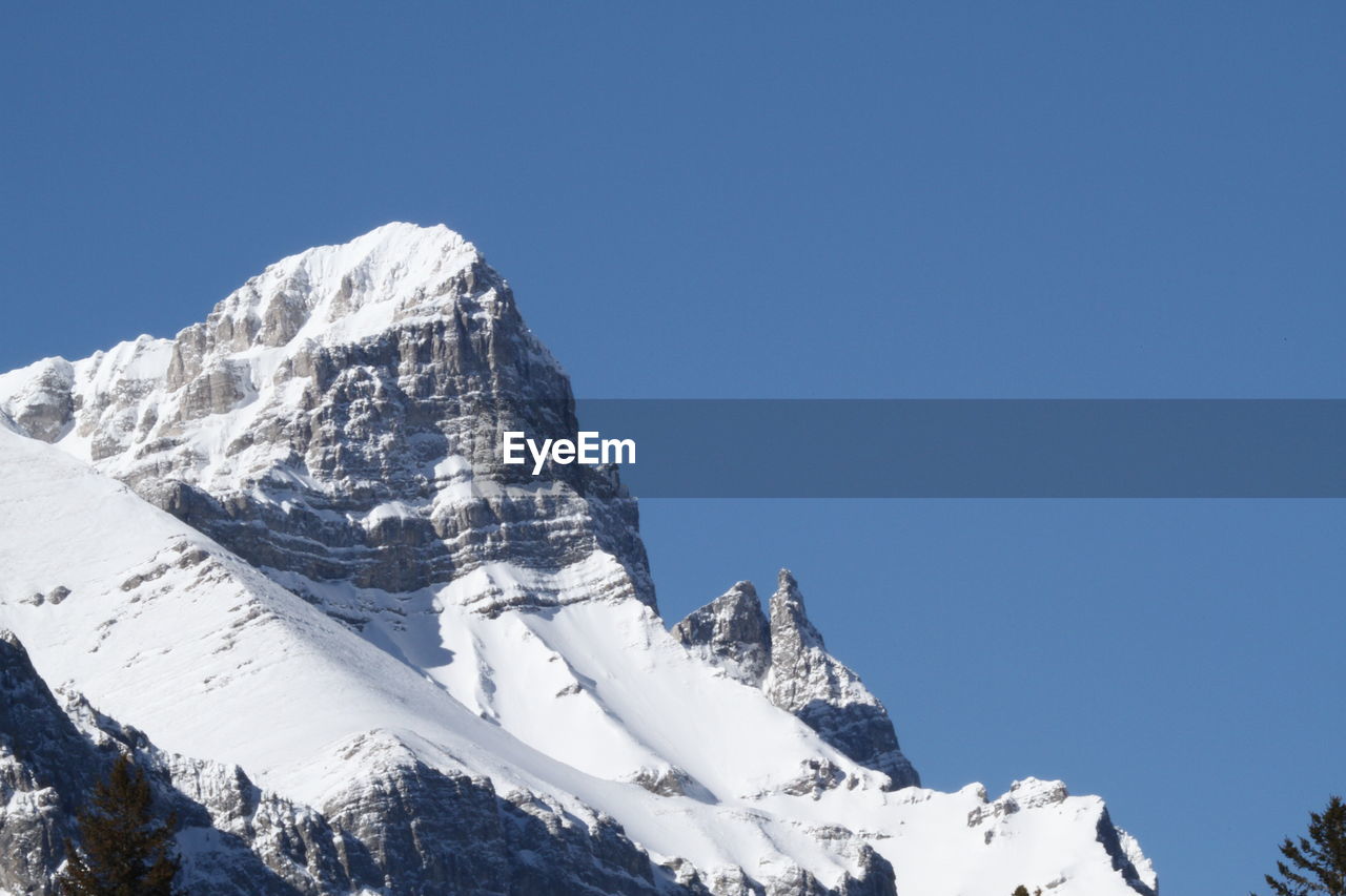 Low angle view of snowcapped mountains against clear blue sky