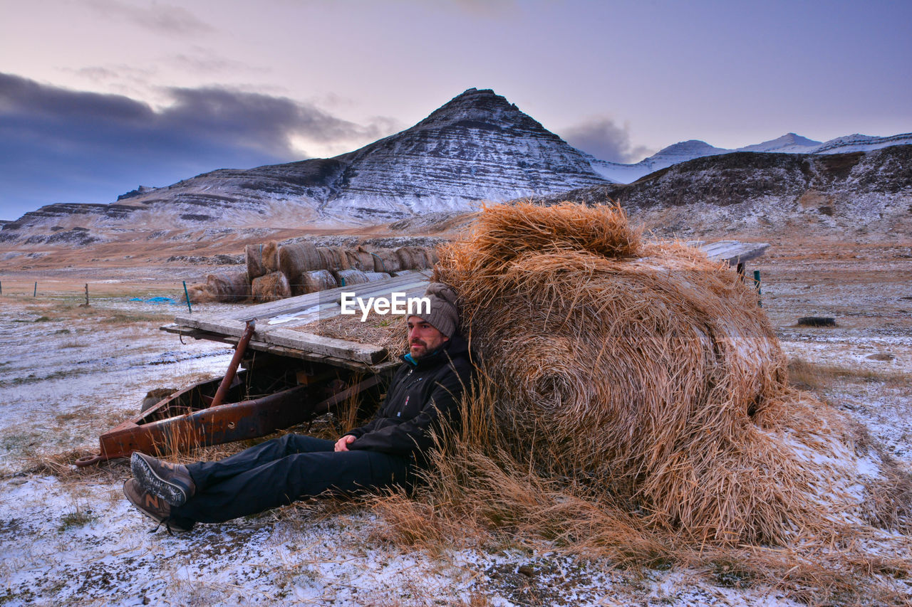 Man looking away while relaxing by hay bale at field