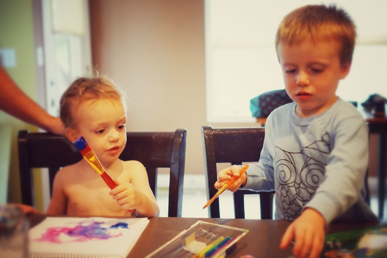 Siblings painting while sitting at table