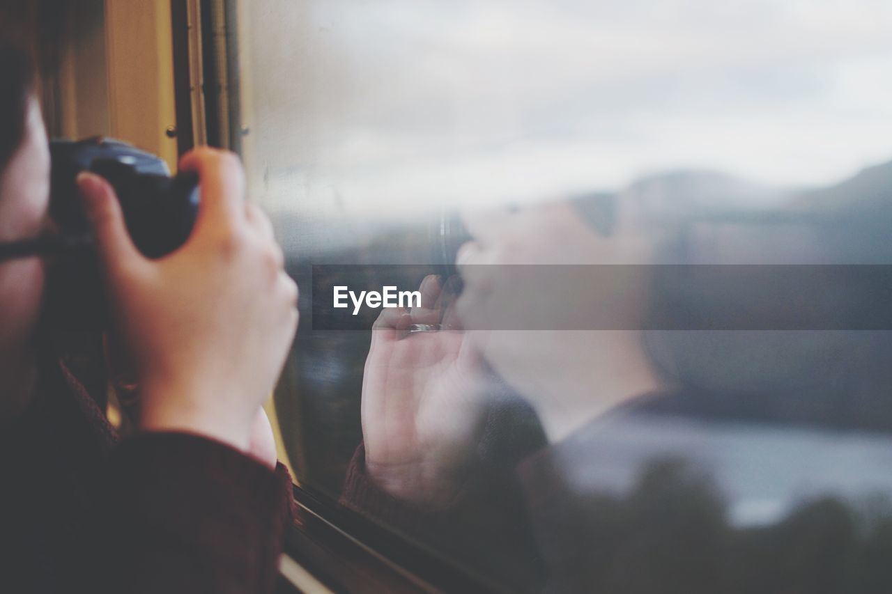 Cropped image of man photographing through camera while sitting in train