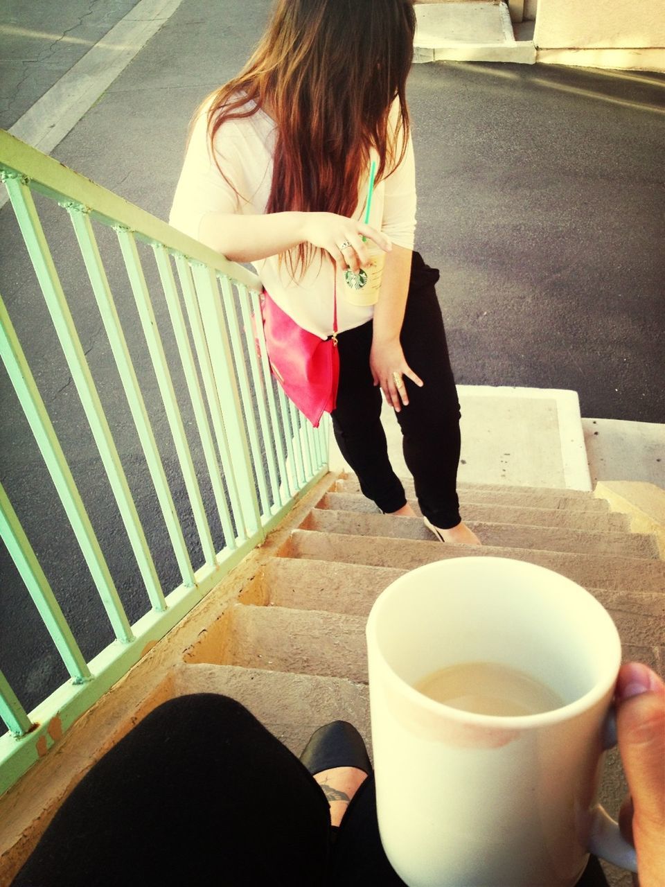 Woman standing on stairs with hand holding coffee cup in foreground