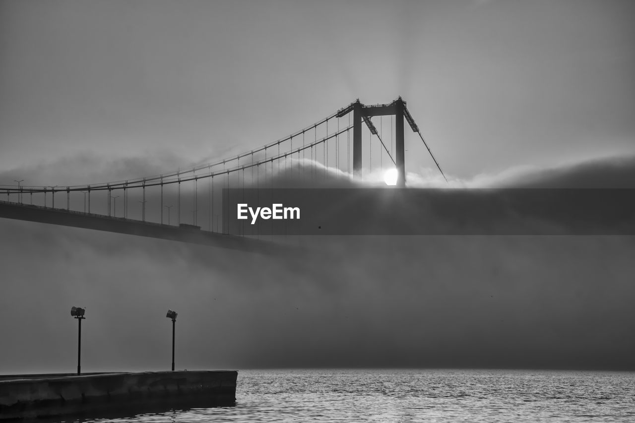 View of suspension bridge against cloudy sky and fog
