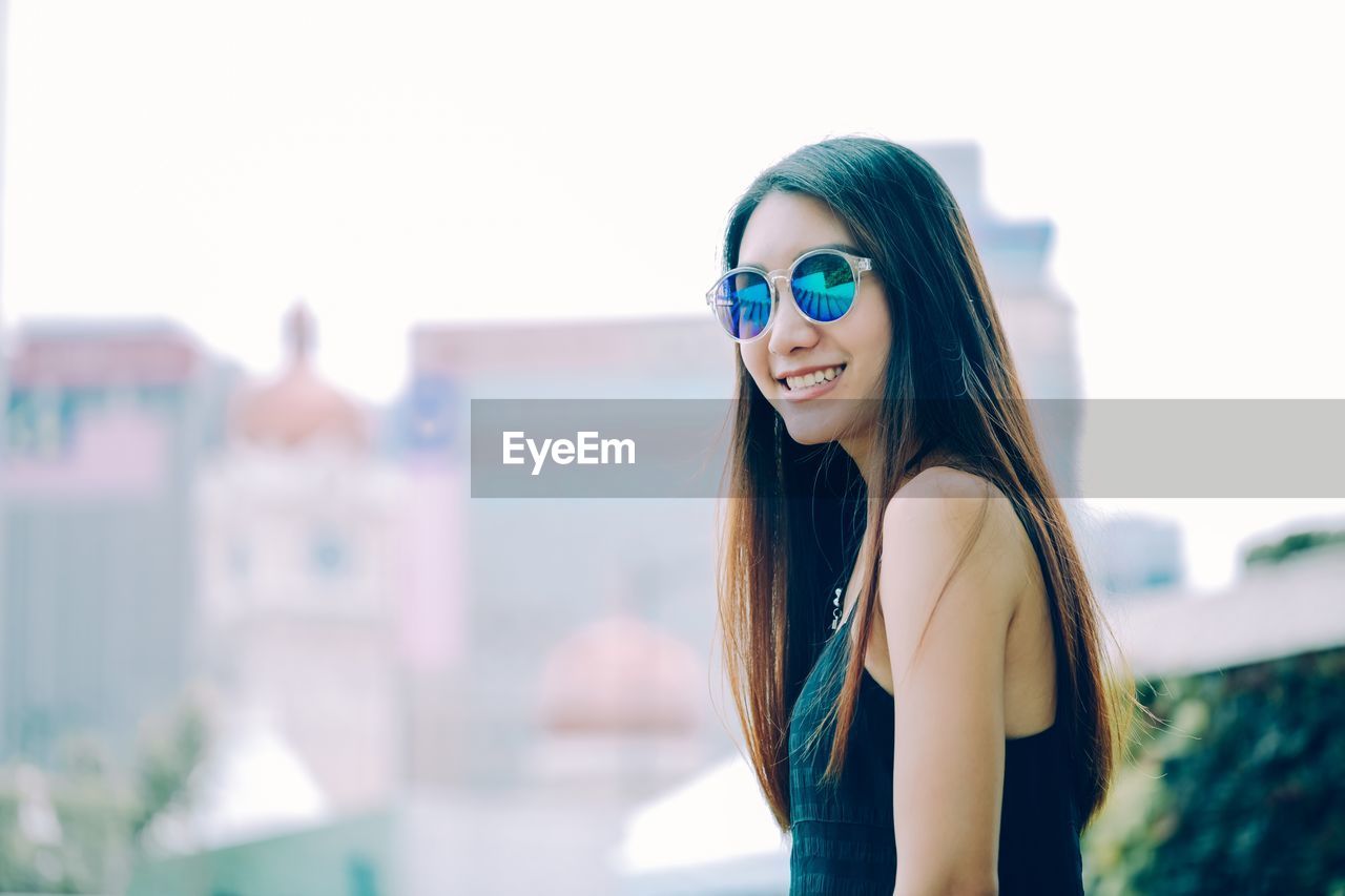 Portrait of smiling young woman standing against clear sky