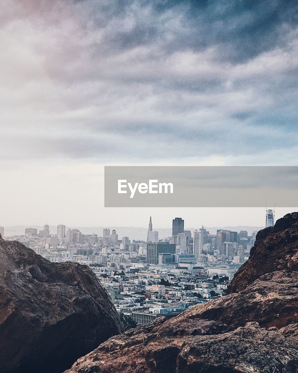 Cityscape seen from mountain against cloudy sky