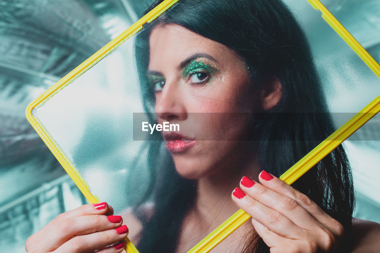 Close-up portrait of woman with make-up seen through glass