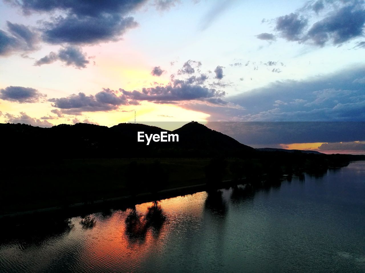 SCENIC VIEW OF LAKE BY SILHOUETTE MOUNTAINS AGAINST SKY AT SUNSET