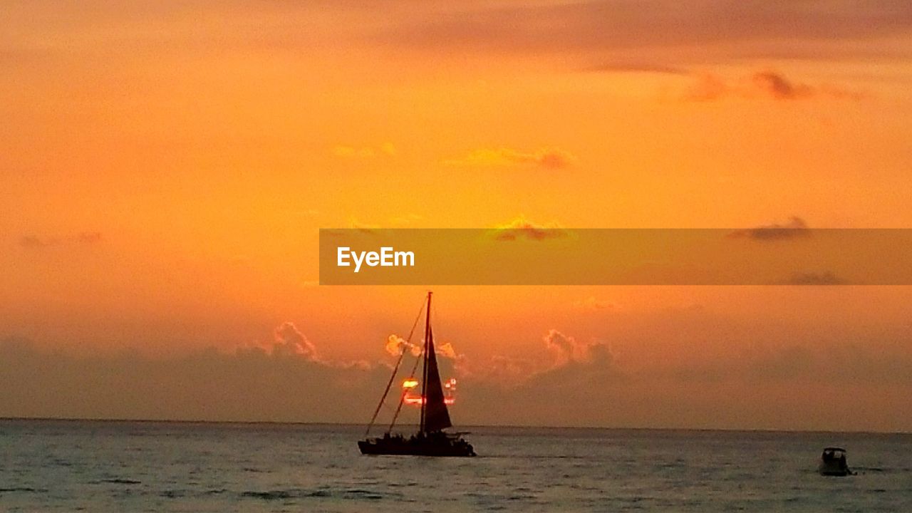 SAILBOAT SAILING IN SEA AT SUNSET