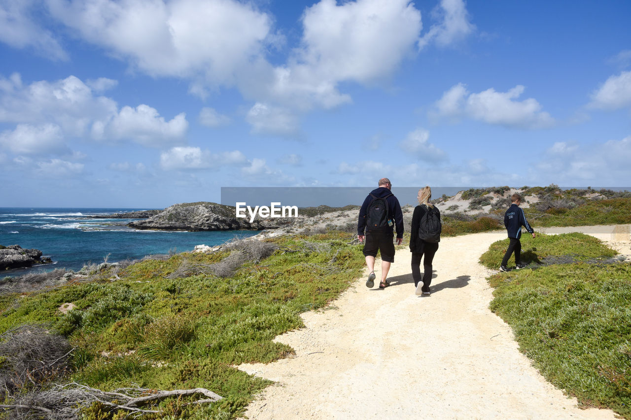 Rear view of people on footpath by sea against sky