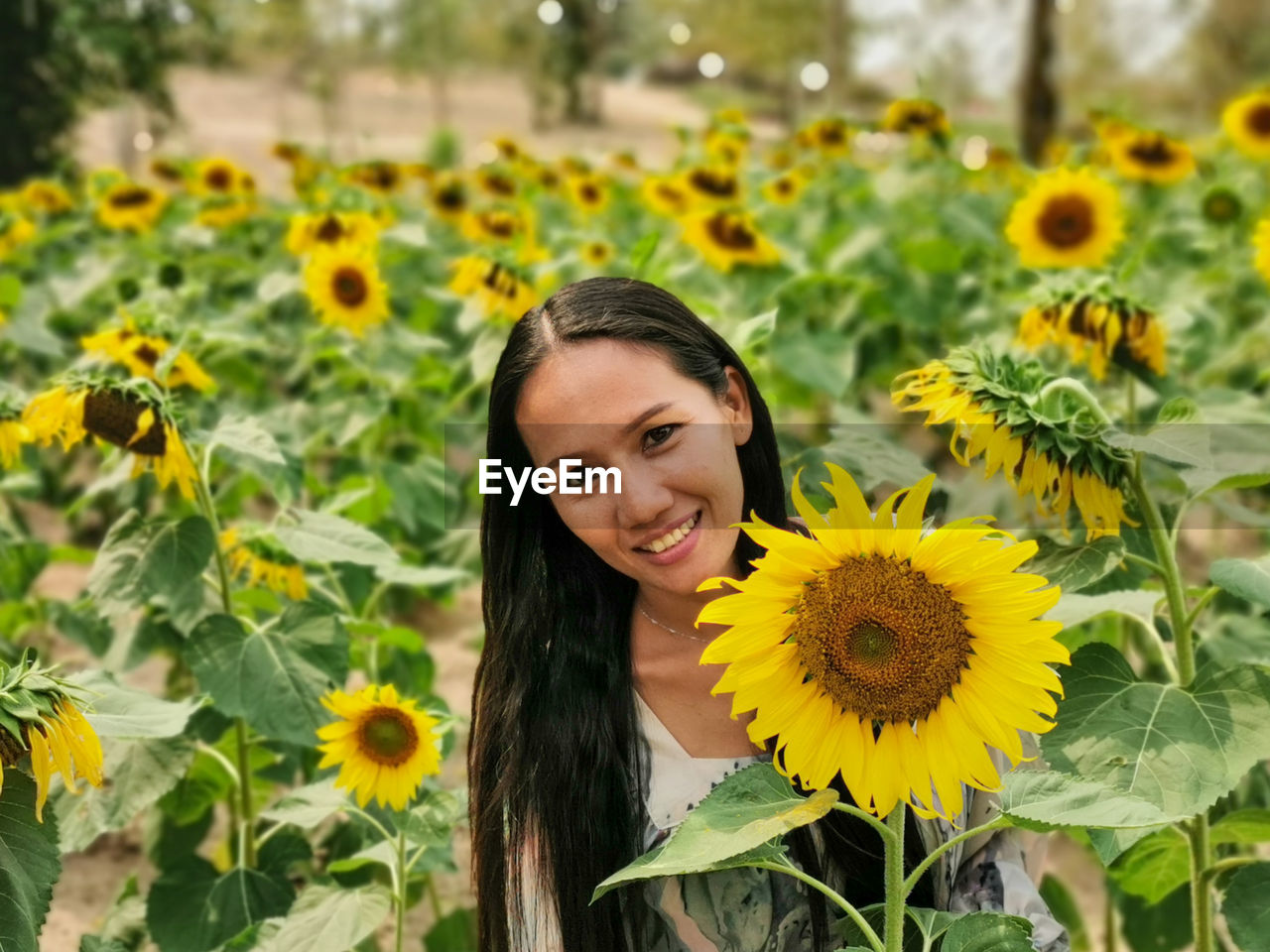 PORTRAIT OF SMILING YOUNG WOMAN AGAINST YELLOW FLOWERING PLANTS