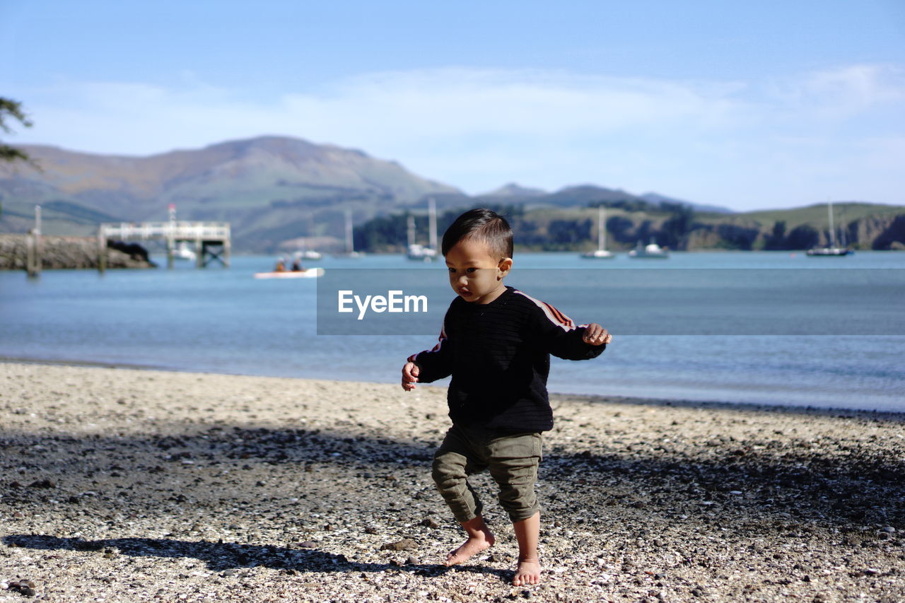 Side view of kid standing at beach against sky