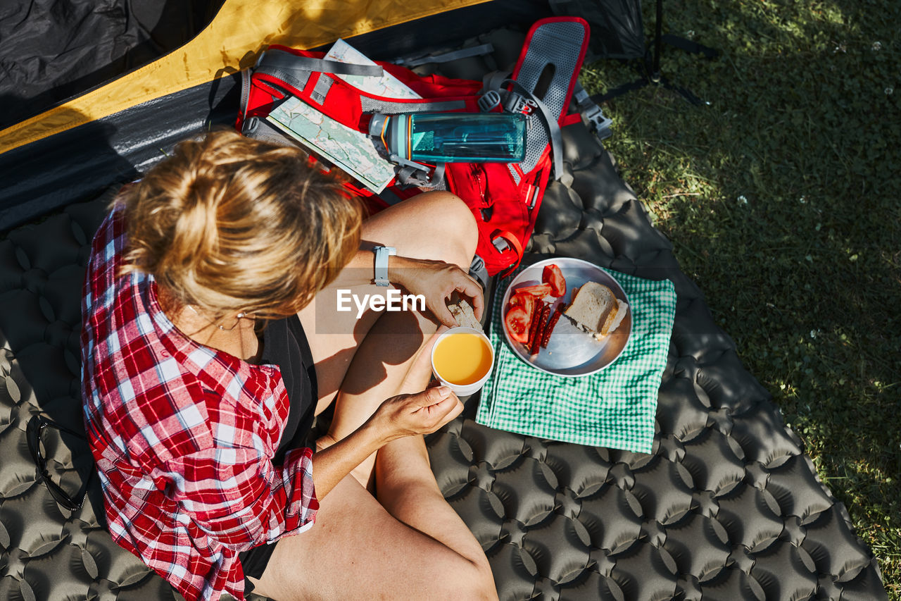 Woman having breakfast sitting by tent at camping. female spending vacations close to nature