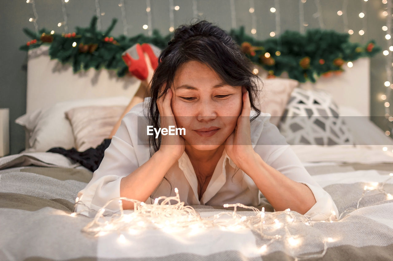 Senior asian woman relax on bed looking at xmas lights, elderly lady at christmas, atmospheric mood