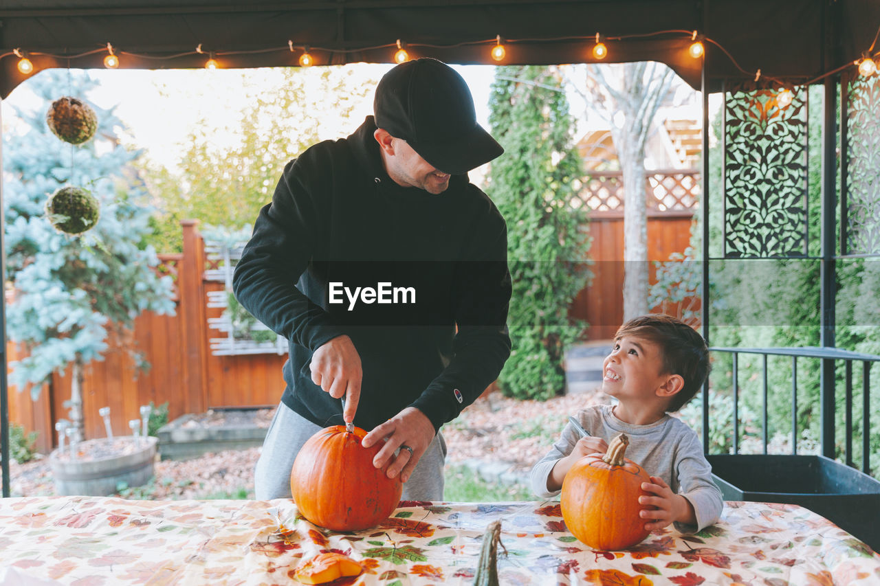 Father and son cutting pumpkin on table