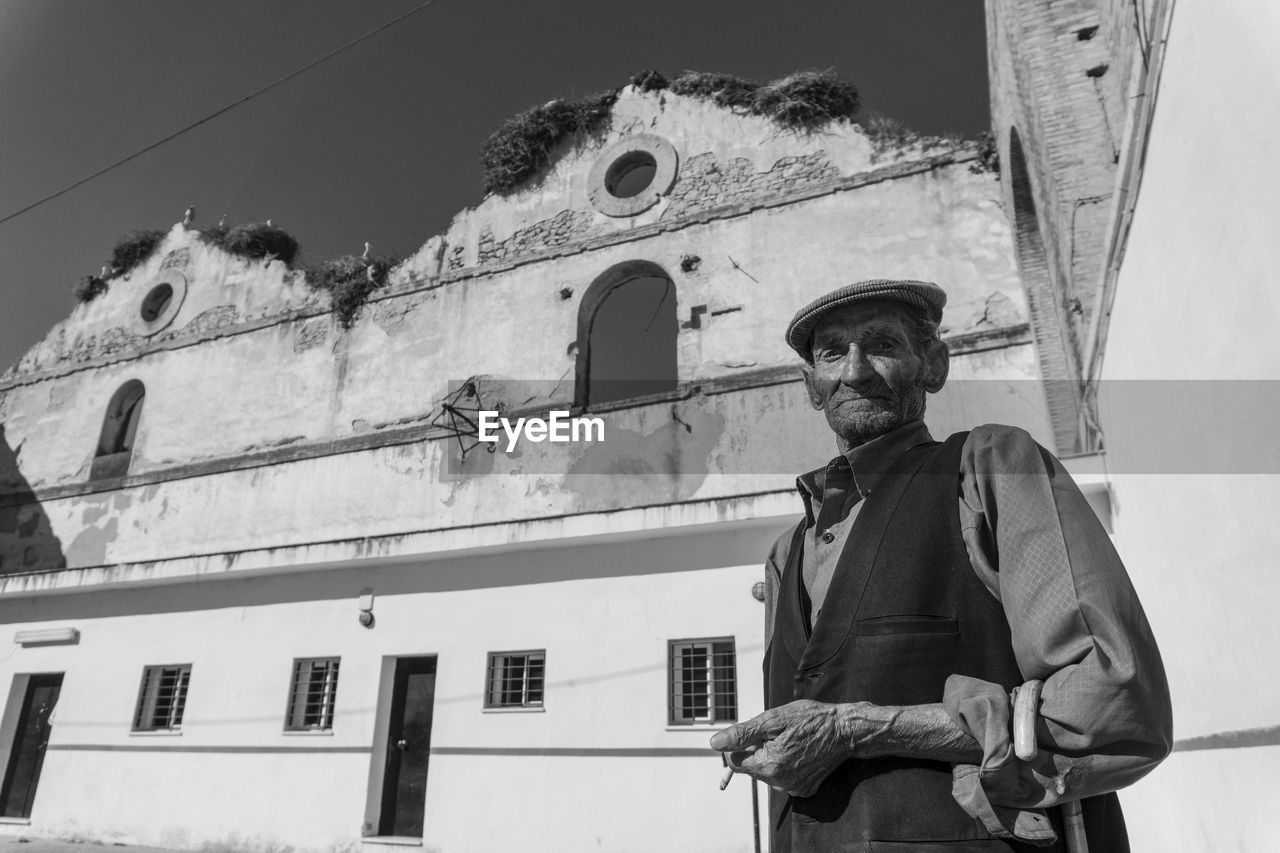 LOW ANGLE VIEW OF MAN STANDING BY BUILDING