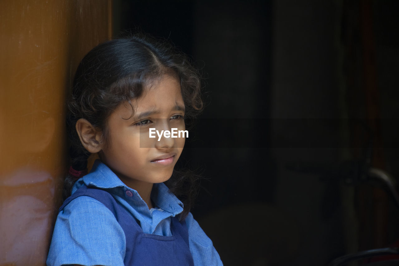 Girl wearing school uniform looking away while standing by wall