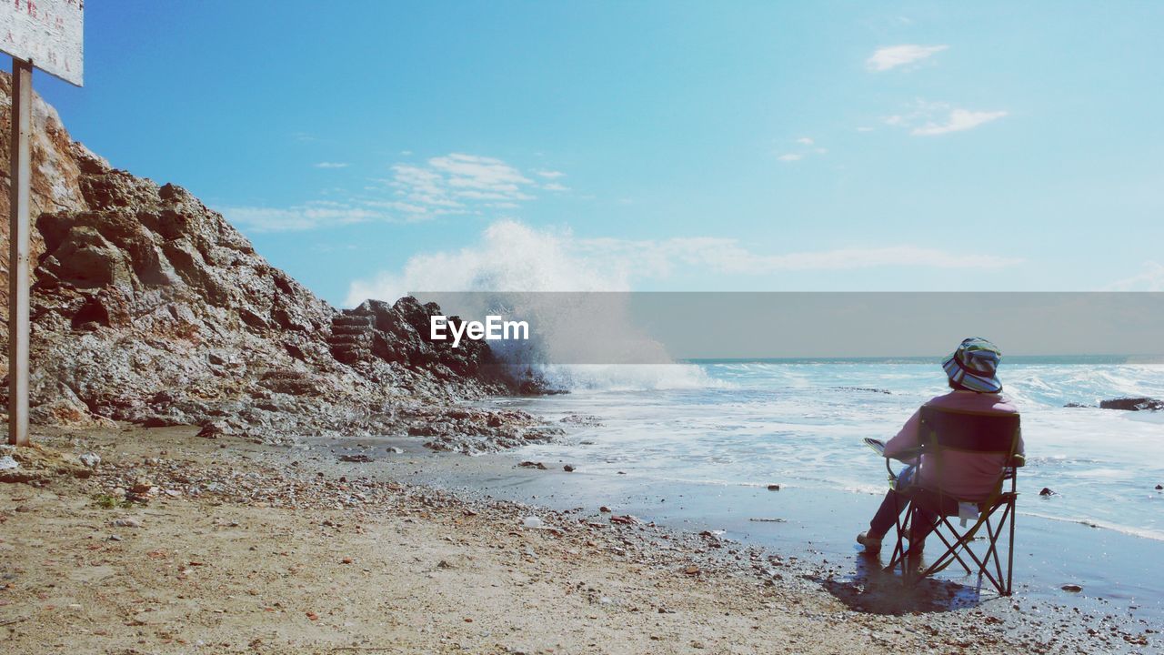 Rear view of person sitting on chair at beach against sky