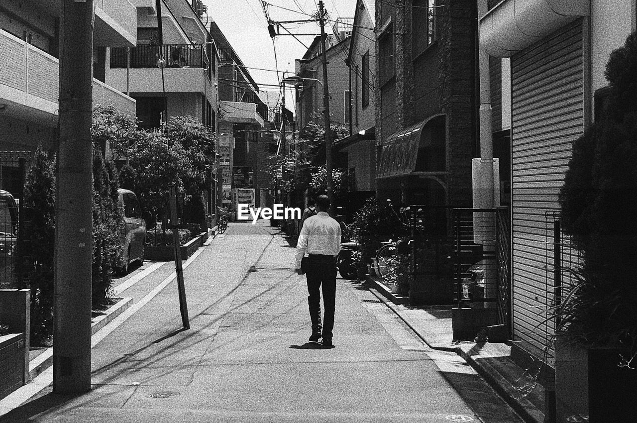 FULL LENGTH REAR VIEW OF MAN WALKING ON STREET IN CITY