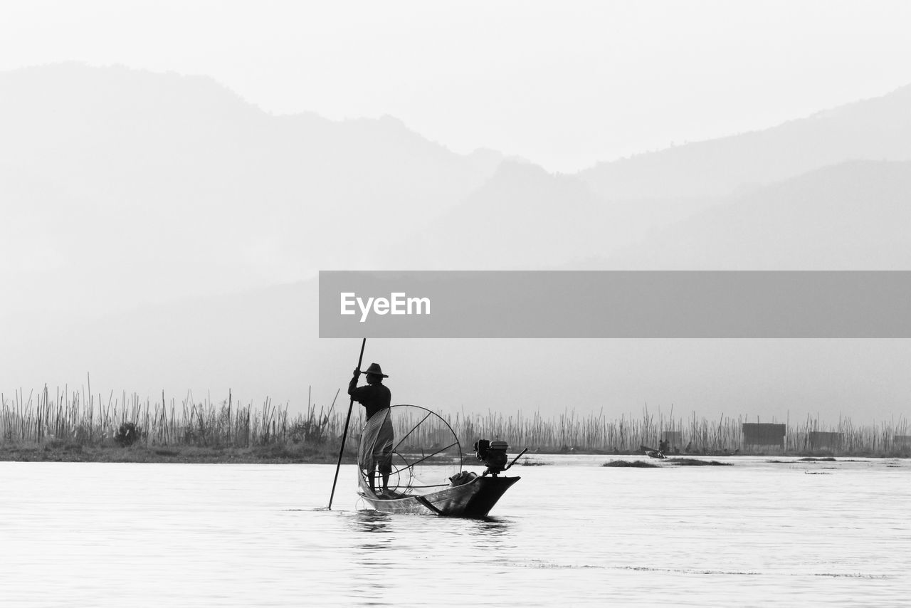 Fisherman standing on boat in lake against sky