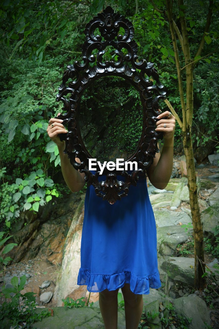 Woman holding mirror with reflection of trees while standing in forest