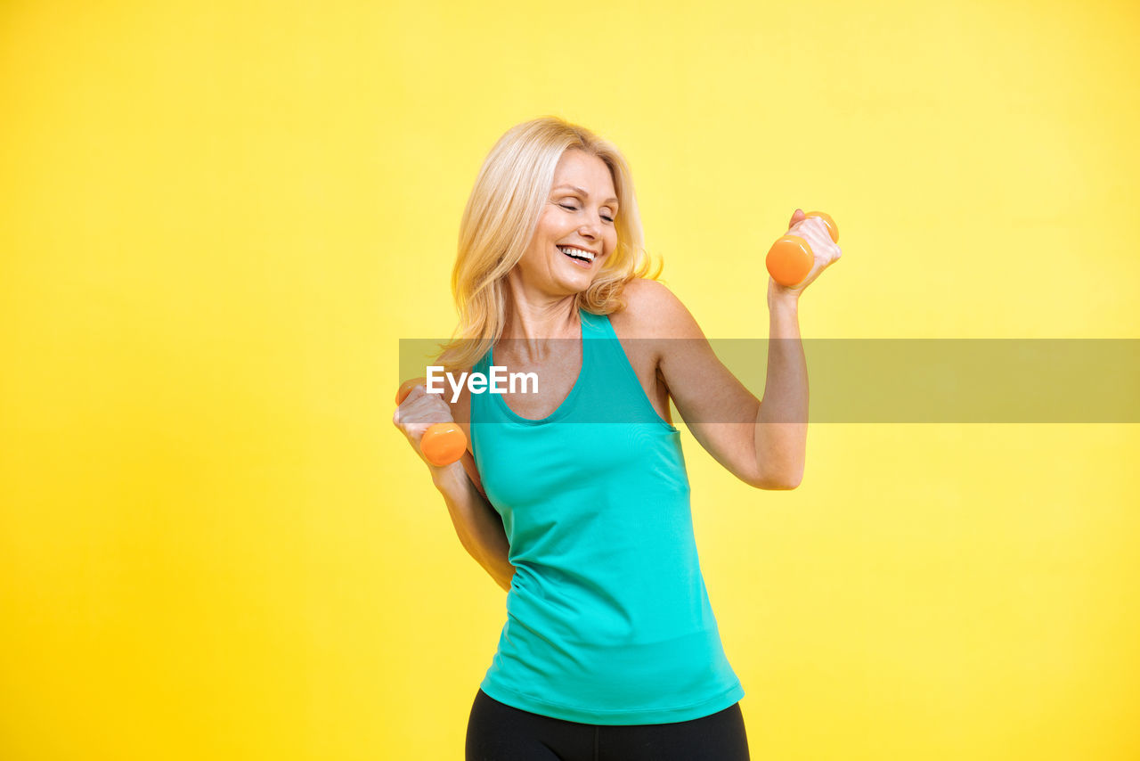 portrait of young woman lifting dumbbell against orange background