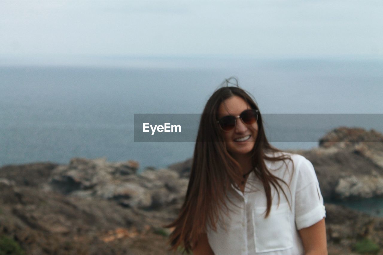 Portrait of woman smiling while standing on rocky shore