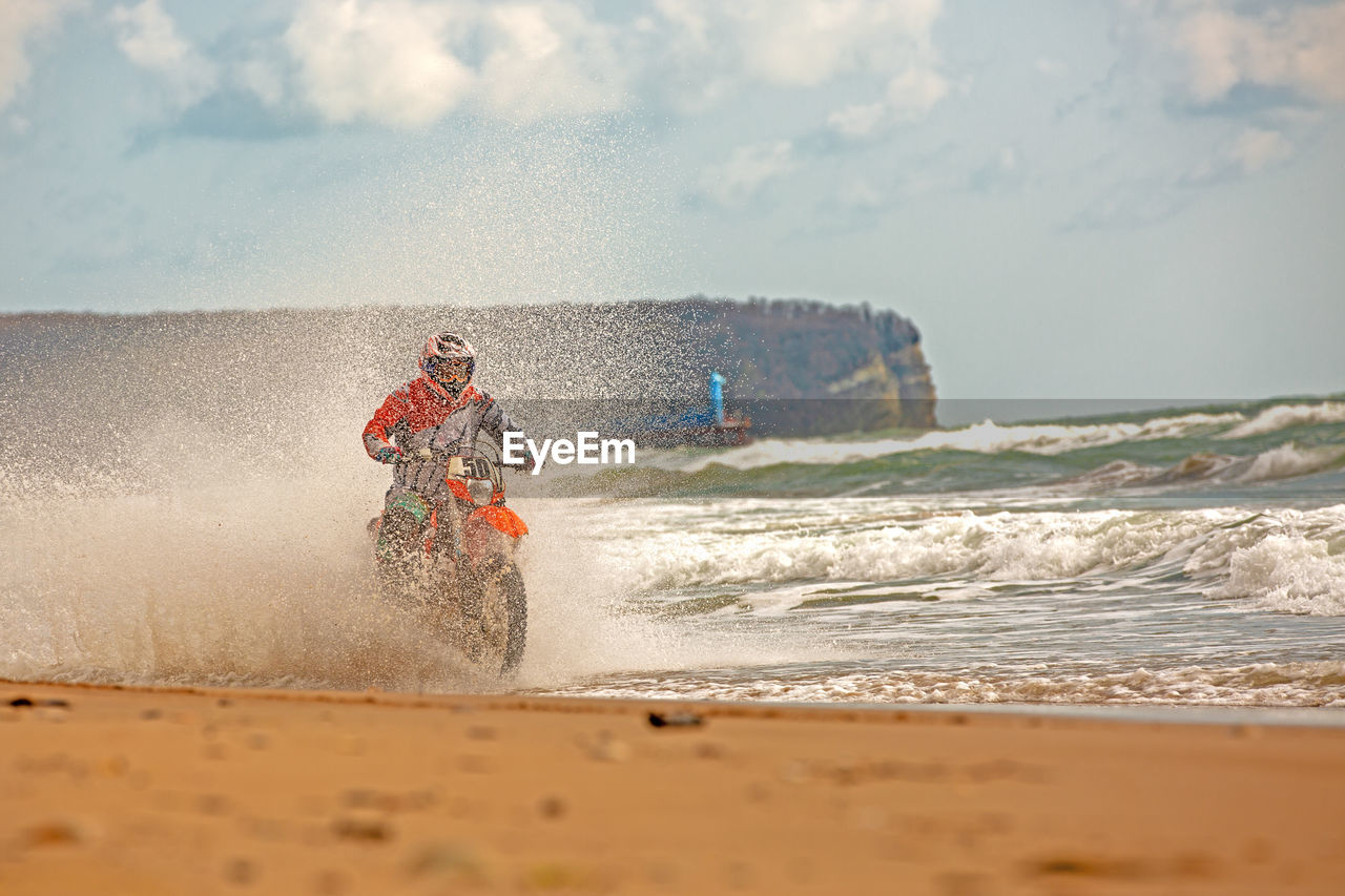 Man riding motorcycle on beach against sky