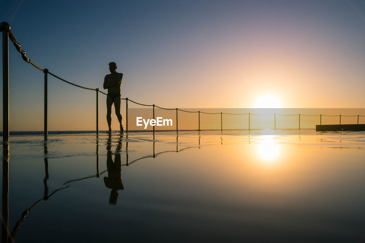 Silhouette of man standing poolside on beach during sunset