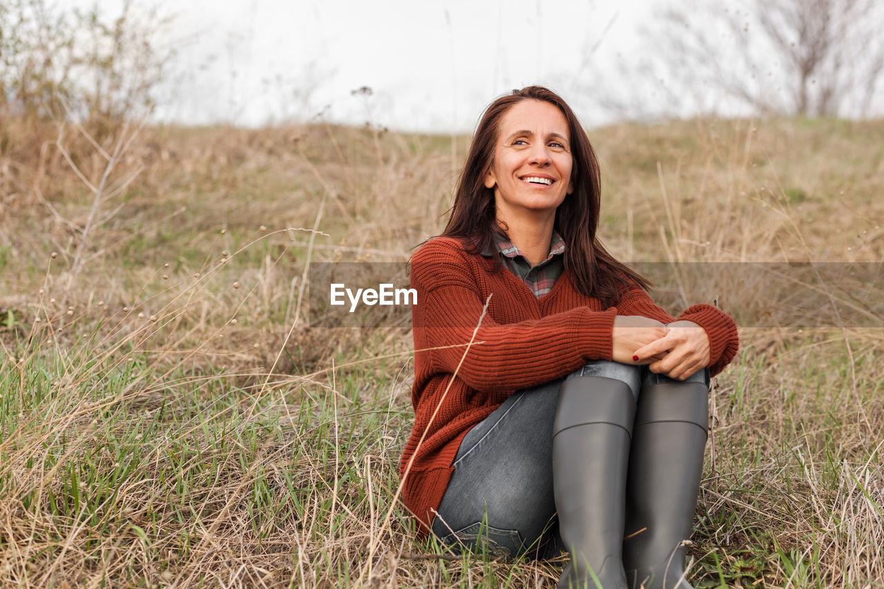 PORTRAIT OF A SMILING YOUNG WOMAN SITTING ON LAND