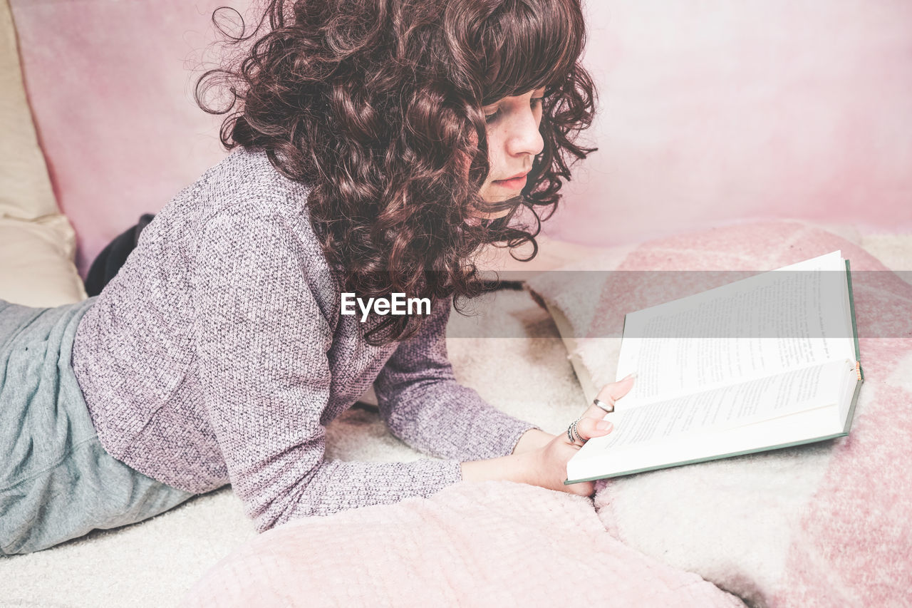 Woman reading book on bed at home