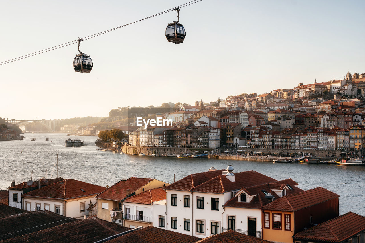 Cable cars hanging over river and cityscape against clear sky