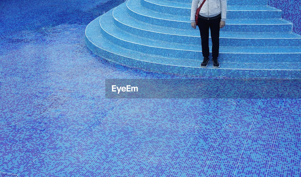 Low section of man standing on steps of empty swimming pool