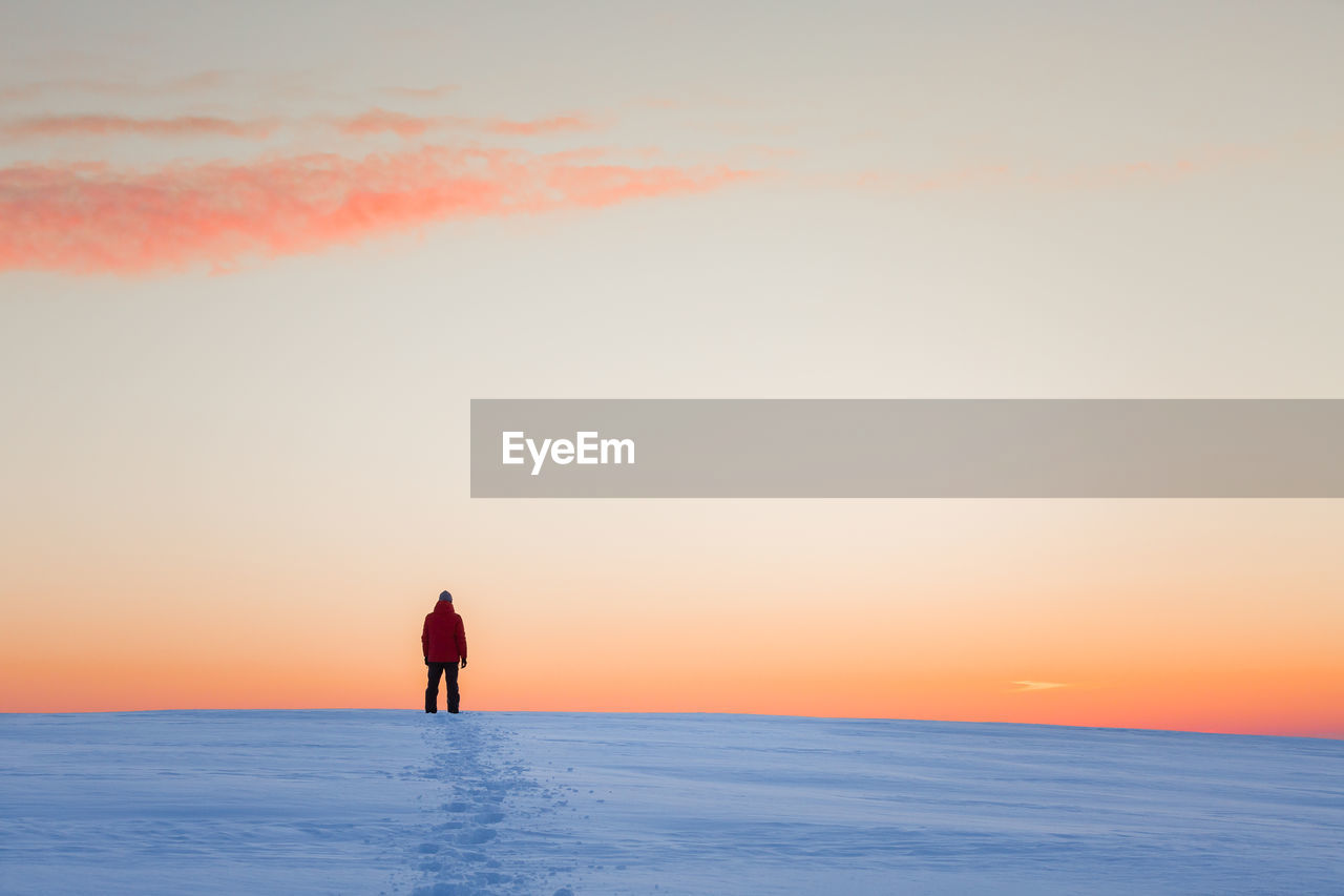 Mid adult man standing on snow covered field against sky during sunset