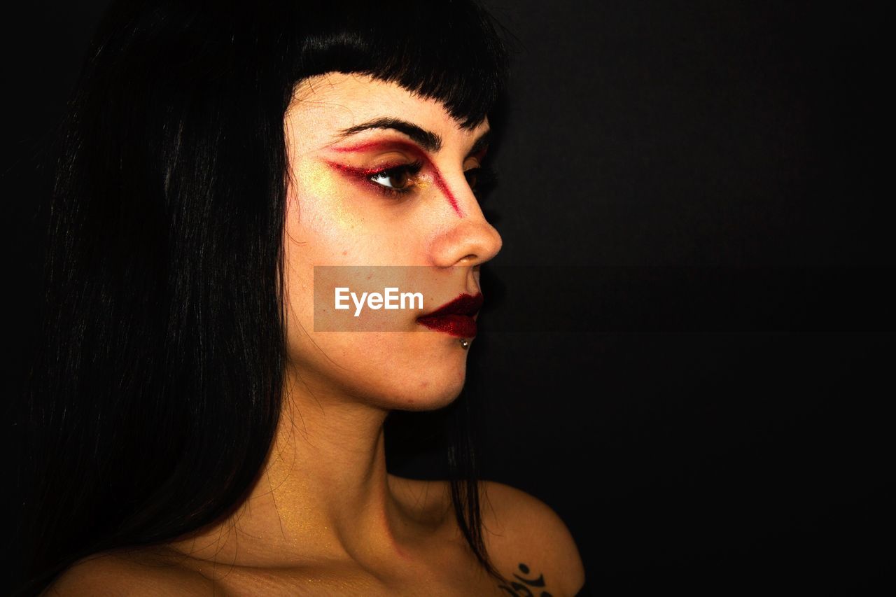 Close-up of woman with red eyeshadow looking away against black background