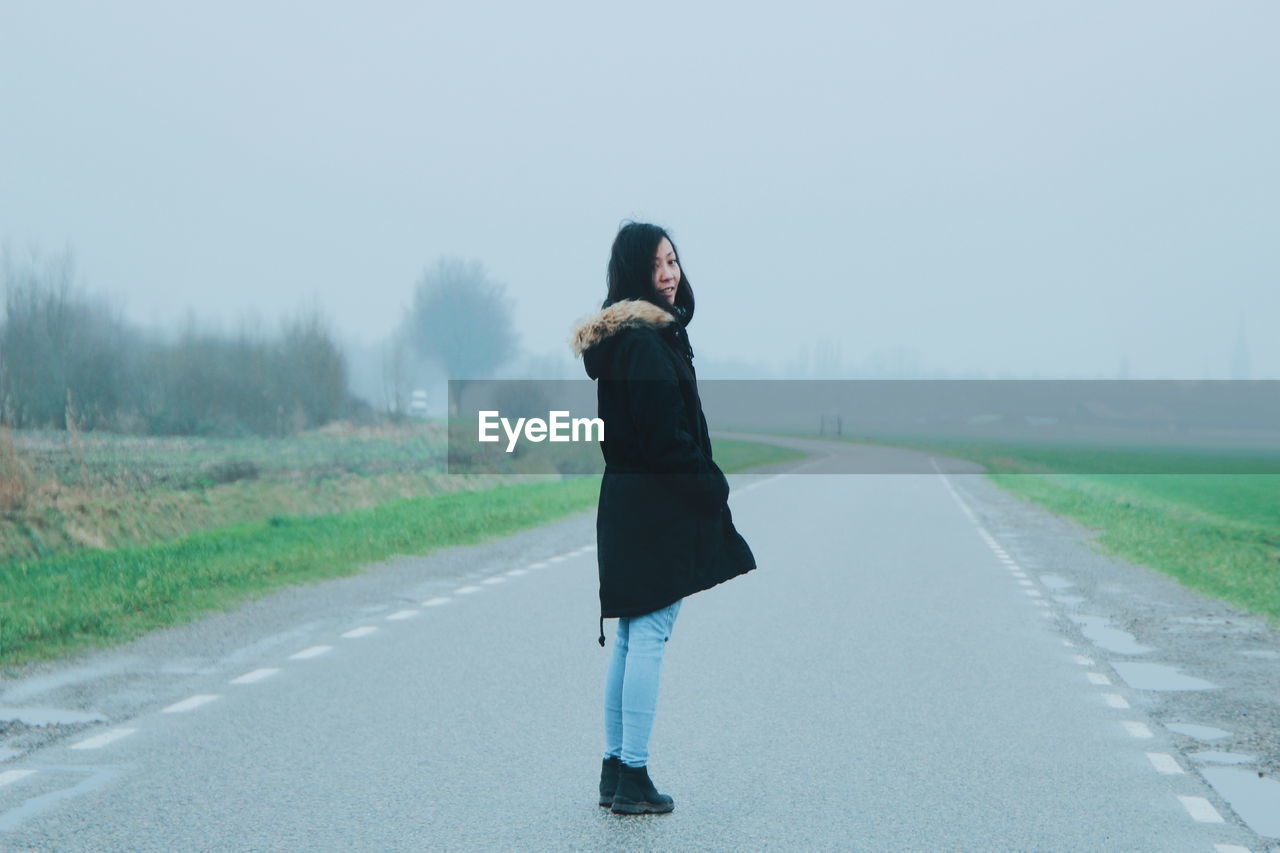 Woman standing on road against sky in foggy weather