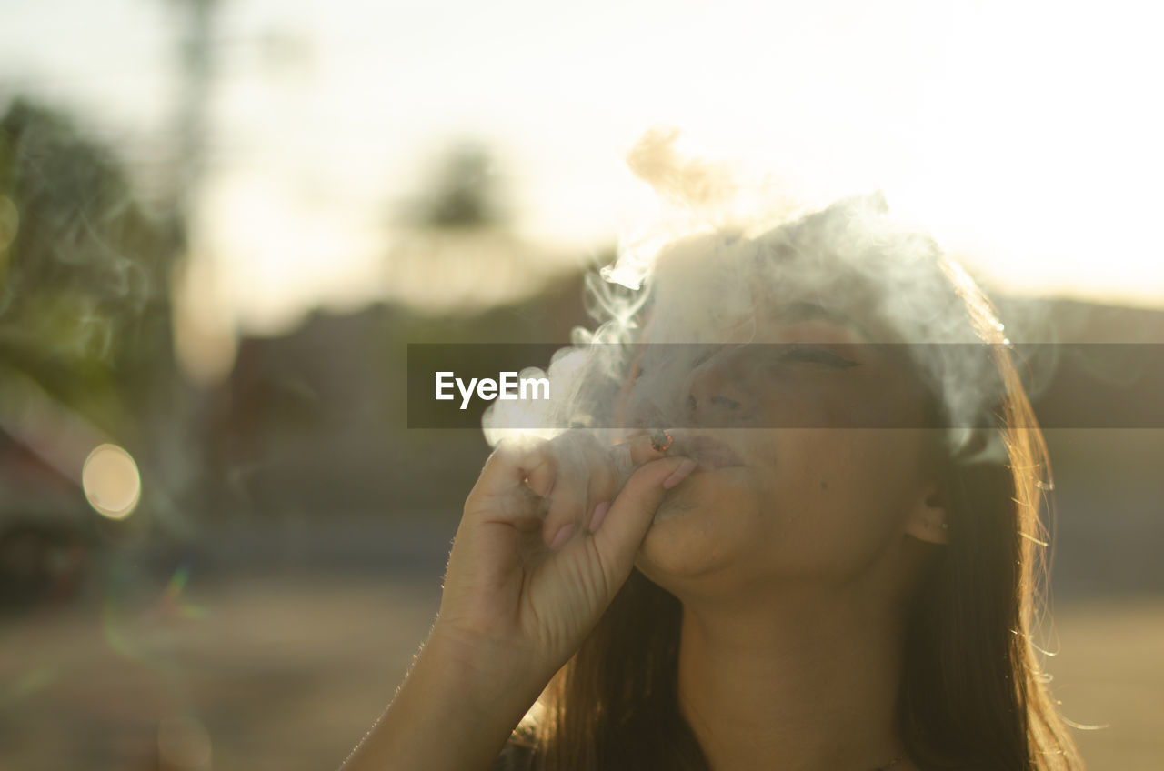 Close-up of young woman smoking against sky