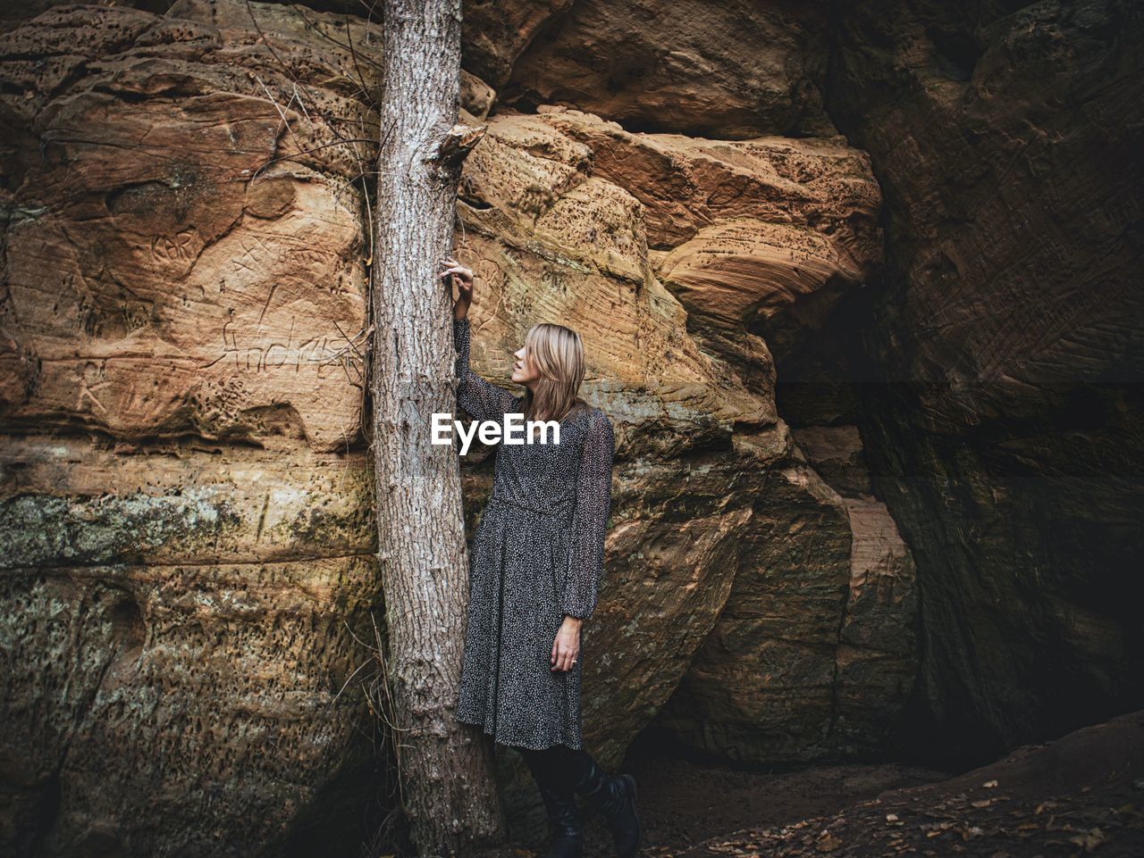 Woman standing on rock against tree trunk