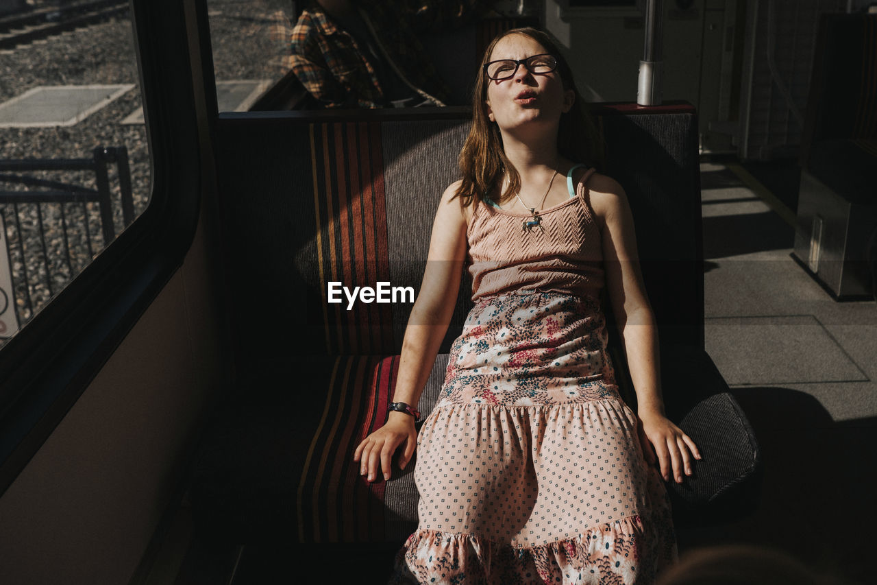 Girl with eyes closed making face while traveling in train