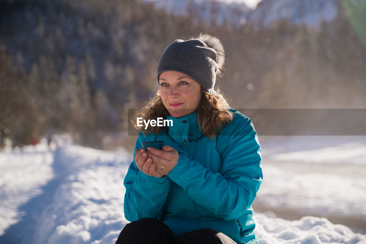 YOUNG WOMAN USING PHONE WHILE STANDING ON SNOW