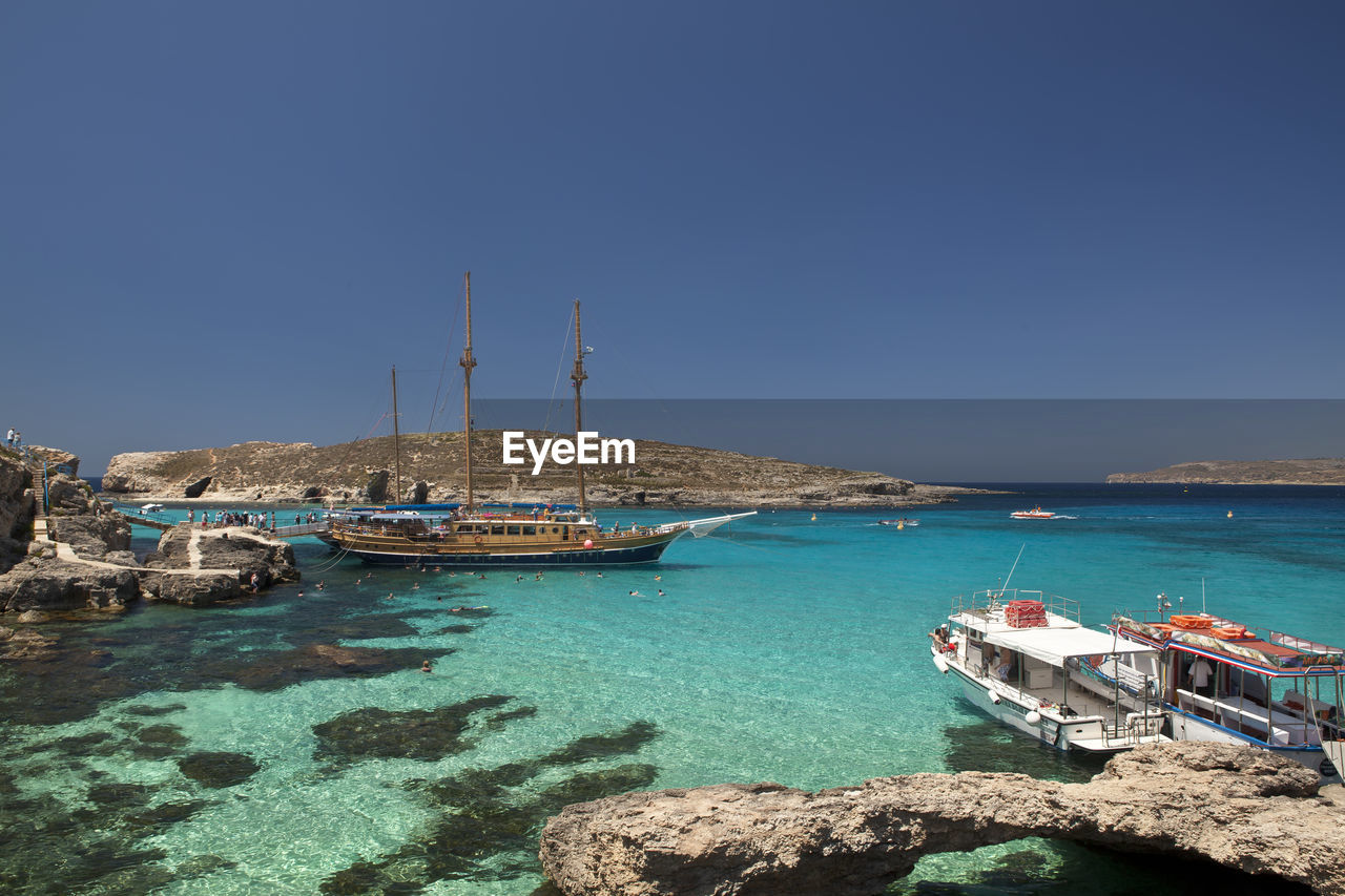 Boats moored on sea against clear blue sky