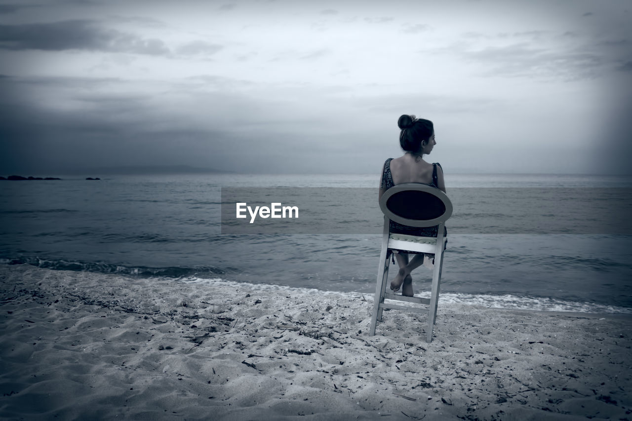 Rear view of woman sitting on chair at beach against sky